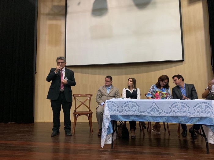 Homem de pé falando enquanto fala com microfone nas mãos 