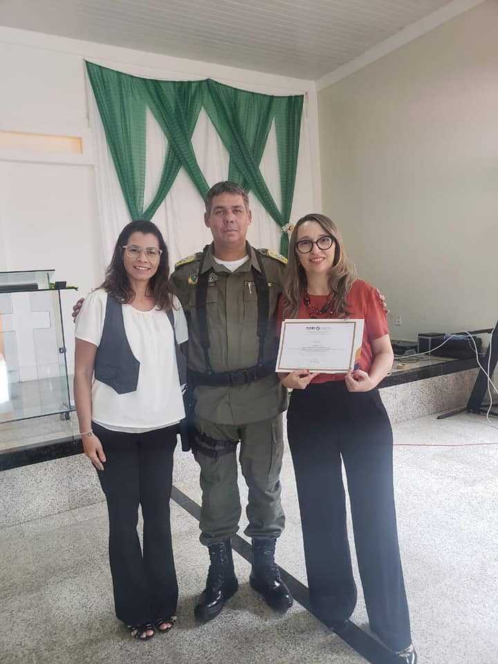 Três pessoas de pé, segurando papel e sorrindo