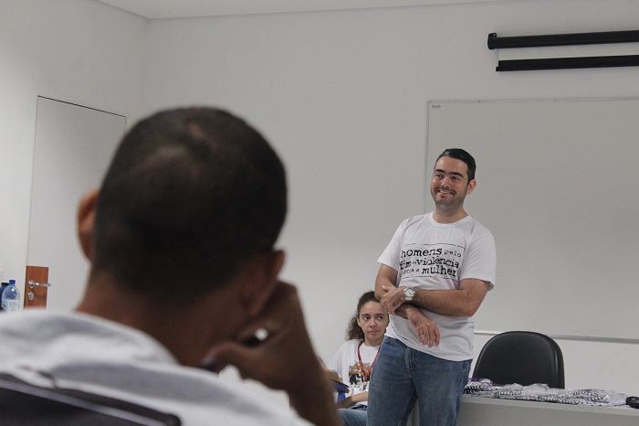 Pessoa de pé falando para um home que está sua frente assentado 