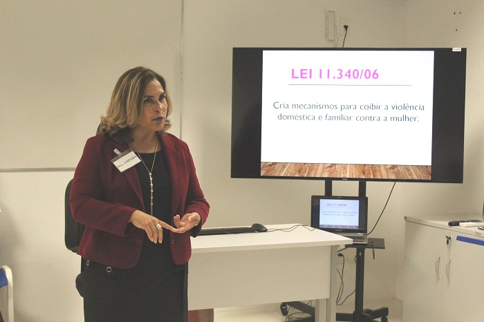 Pessoa de pé falando para o público que a observa 