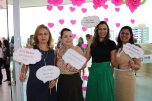 Mulheres de pé sorrindo e segurando plaquinhas com dizeres sobre o que é ser mãe
