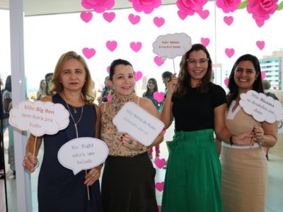 Mulheres de pé sorrindo e segurando plaquinhas com dizeres sobre o que é ser mãe