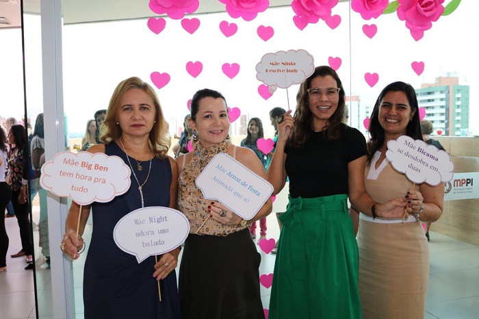 Mulheres de pé sorrindo e segurando plaquinhas com dizeres sobre o que é ser mãe