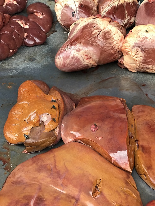 Fotos de carnes expostas em balcão com moscas em cima das carnes