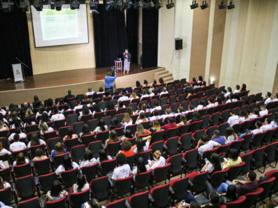 Estudantes observam slide exibido ao fundo da imagem