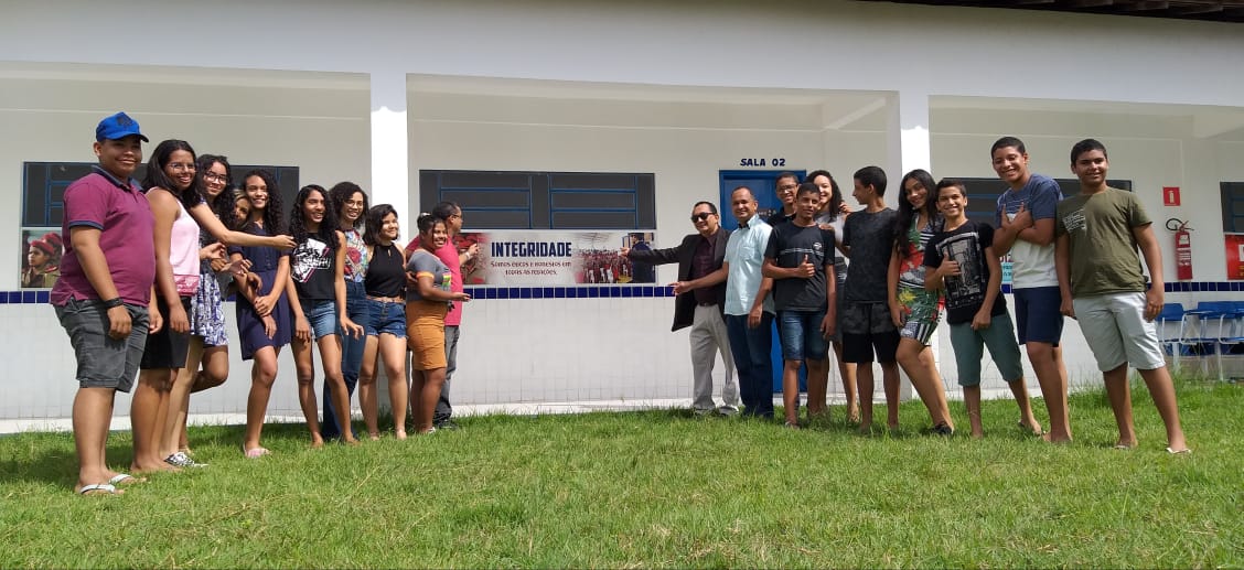 Promotor de Justiça com estudantes em gramado, diante de um banner em que se lê a palavra integridade