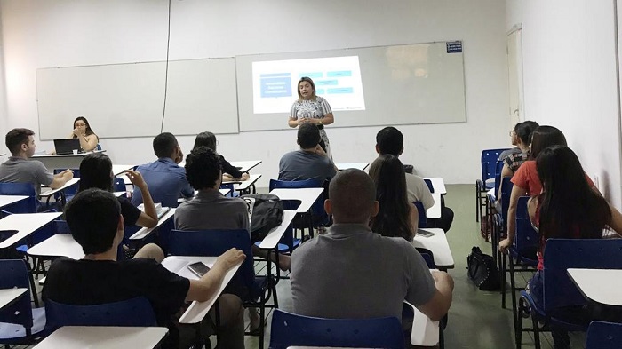 Mulher falando para plateia de sala de aula