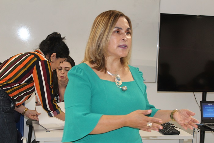 Pessoa de pé falando para o público que está sentado a sua frente 