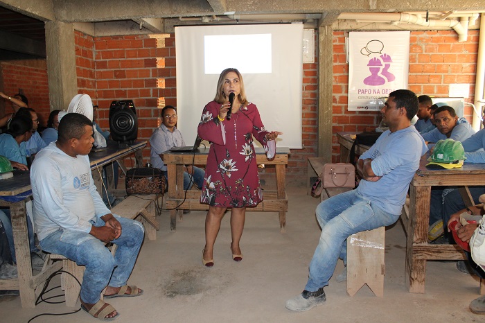 Pessoas sentadas observando uma mulher de pé falando 