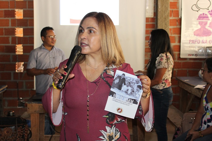 MUlher de pé falando para o público e segurando um microfone 