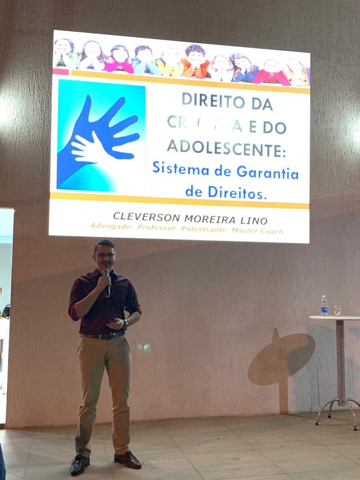 Pessoa de pé falando com o público a sua frente 