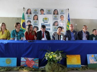 Pessoas sentadas em uma mesa de honra durante solenidade