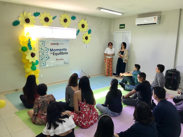 duas mulheres de pé e pessoas sentadas no chão