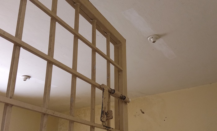 Foto de uma cela do CEM. Na foto uma parte da grade da porta ao fundo o teto sem lâmpada 