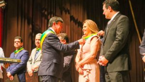 Momento que o Governador do Piauí, Wellington Dias, entrega medalha para a PGJ Carmelina moura. Ela sorri e olha para frente enquanto recebe a honraria.