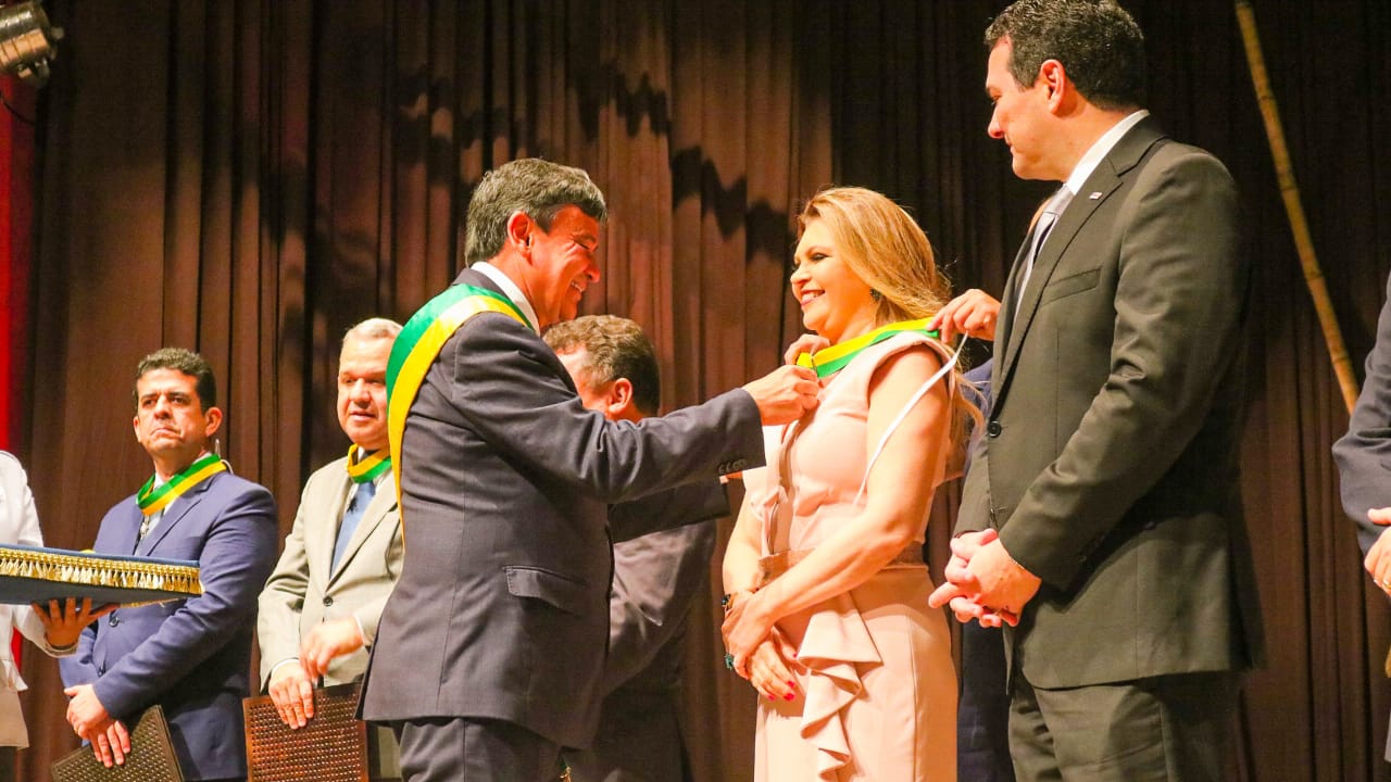 Momento que o Governador do Piauí, Wellington Dias, entrega medalha para a PGJ Carmelina moura. Ela sorri e olha para frente enquanto recebe a honraria.