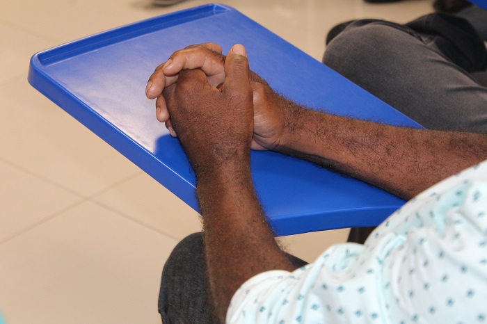 Pessoa sentada em uma cadeira e com as mãos sobre uma mesa 