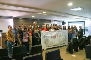 Pessoas segurando uma faixa em que estão impressos os fluxos de atendimento