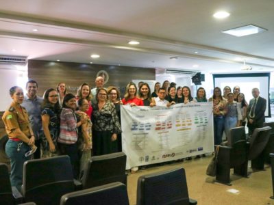 Pessoas segurando uma faixa em que estão impressos os fluxos de atendimento