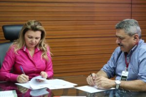 Mulher assinando documento e homem observando o gesto