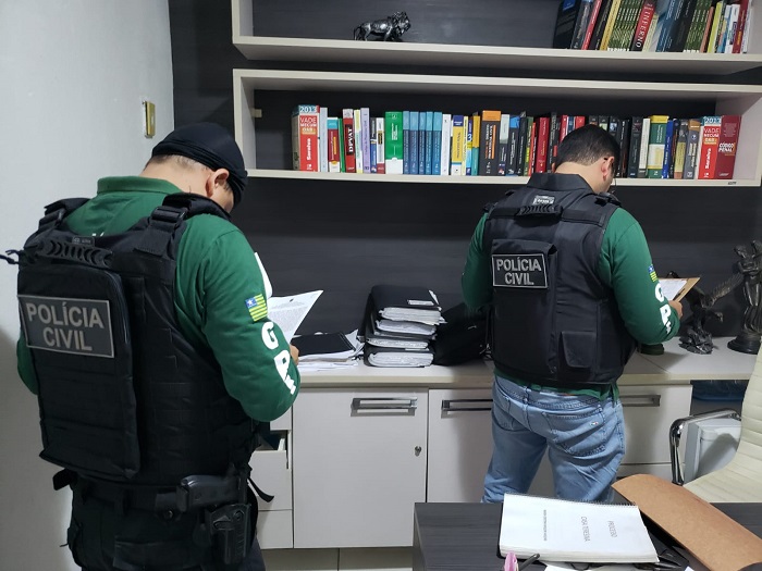Pessoas de pé olhando documentos que estão sobre duas mesas 