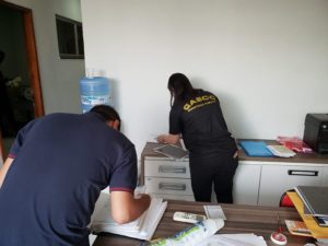 Pessoas olhando documentos que estão sobre bancadas e mesas