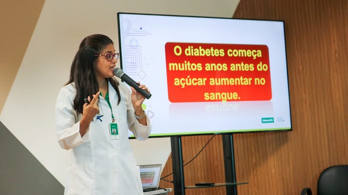 Pessoa de pé ao lado de uma tela com informações sobre o diabetes 