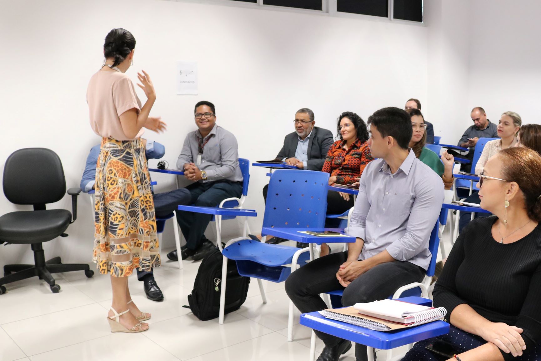 Mulher em pé falando para pessoas sentadas