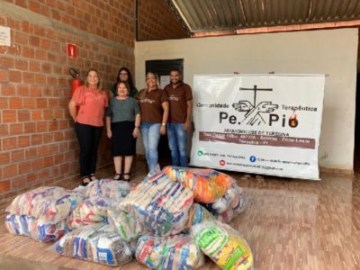 Pessoas de pé em frente aos alimento obtidos com a arrecadação