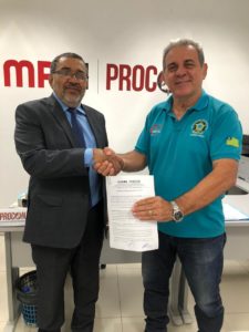 Dois homens em pé segurando documento e apertando as mãos
