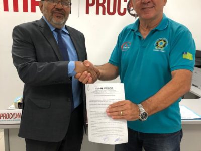 Dois homens em pé segurando documento e apertando as mãos