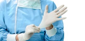 Foto de uma pessoa com avental colocando um luva de látex numa das mãos