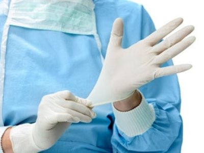 Foto de uma pessoa com avental colocando um luva de látex numa das mãos