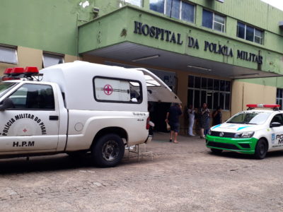 Fachada do Hospital da Polícia Militar com âmbulância e carro da Polícia estacionados em frente