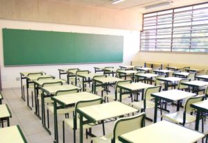 Sala de aula com lousa ao fundo e carteiras enfileiradas