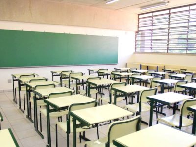 Sala de aula com lousa ao fundo e carteiras enfileiradas