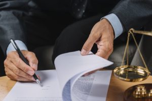 Mão de uma pessoa assinando um documento sobre uma mesa